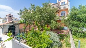 A residential area with a two-story house, a covered patio, and a garden with various plants and flowers. - Apartment in Vodice with Terrace, Air condition, WIFI (4441-3) (Vodice)