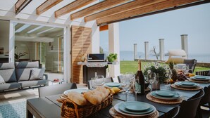 Een terras buiten met uitzicht op zee, een barbecue en een gezellige zithoek.