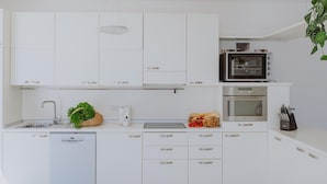 Een moderne keuken met witte kastjes, een magnetron, een oven en een vaatwasser.