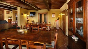 A dining area with a wooden table and chairs, a television mounted on the wall, and a cabinet with glassware. - Villa in Montecatini with 11 bedrooms sleeps 22 (Montecatini)