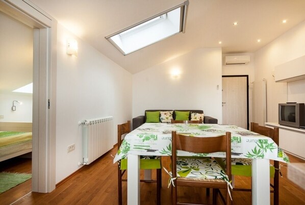 A compact room with a dining table, chairs, a bed, a radiator, a TV, and a skylight.