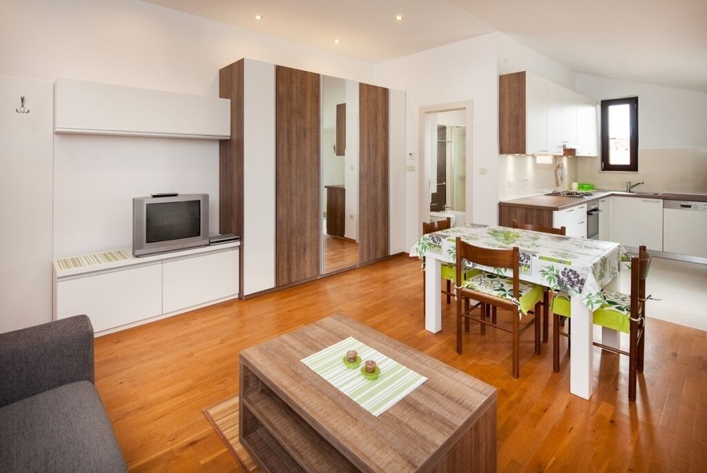 A modern living room with a sofa, a wooden coffee table, and a dining area with a table and chairs. There is a kitchen area with cabinets and a sink.