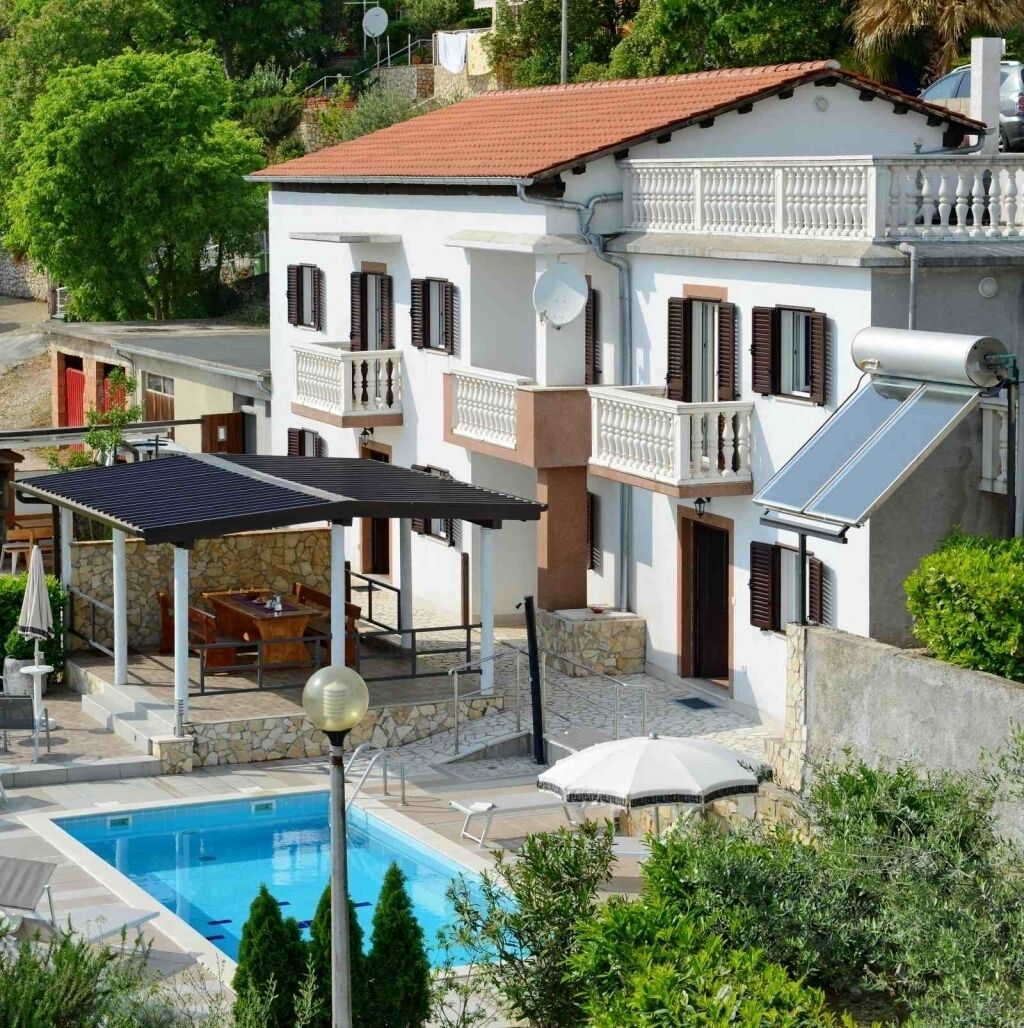 A two-story house with a swimming pool, outdoor seating, and solar panels.