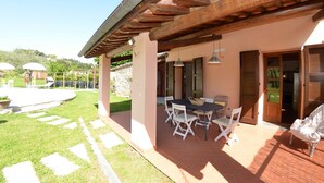Un patio al aire libre con una mesa y sillas, un muro de piedra y vistas a un jardín y colinas al fondo.
