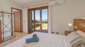 A bedroom with a bed, a nightstand, a lamp, a wardrobe, and a sliding glass door leading to a balcony.