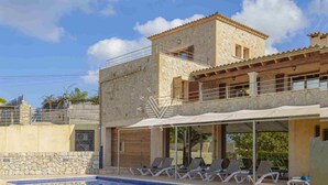 A two-story house with a swimming pool, outdoor seating, and a stone facade.