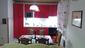 A dining area with a table set for four, red kitchen cabinets, a microwave, and a window with curtains. - Apartment in Kožino with Seaview, Balcony, Air condition, WIFI (4262-1) (Kožino)