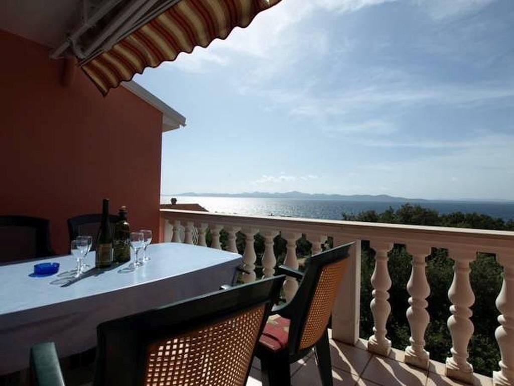 Ein Balkon mit Esstisch, mit Blick auf eine malerische Landschaft aus Meer und Bergen.