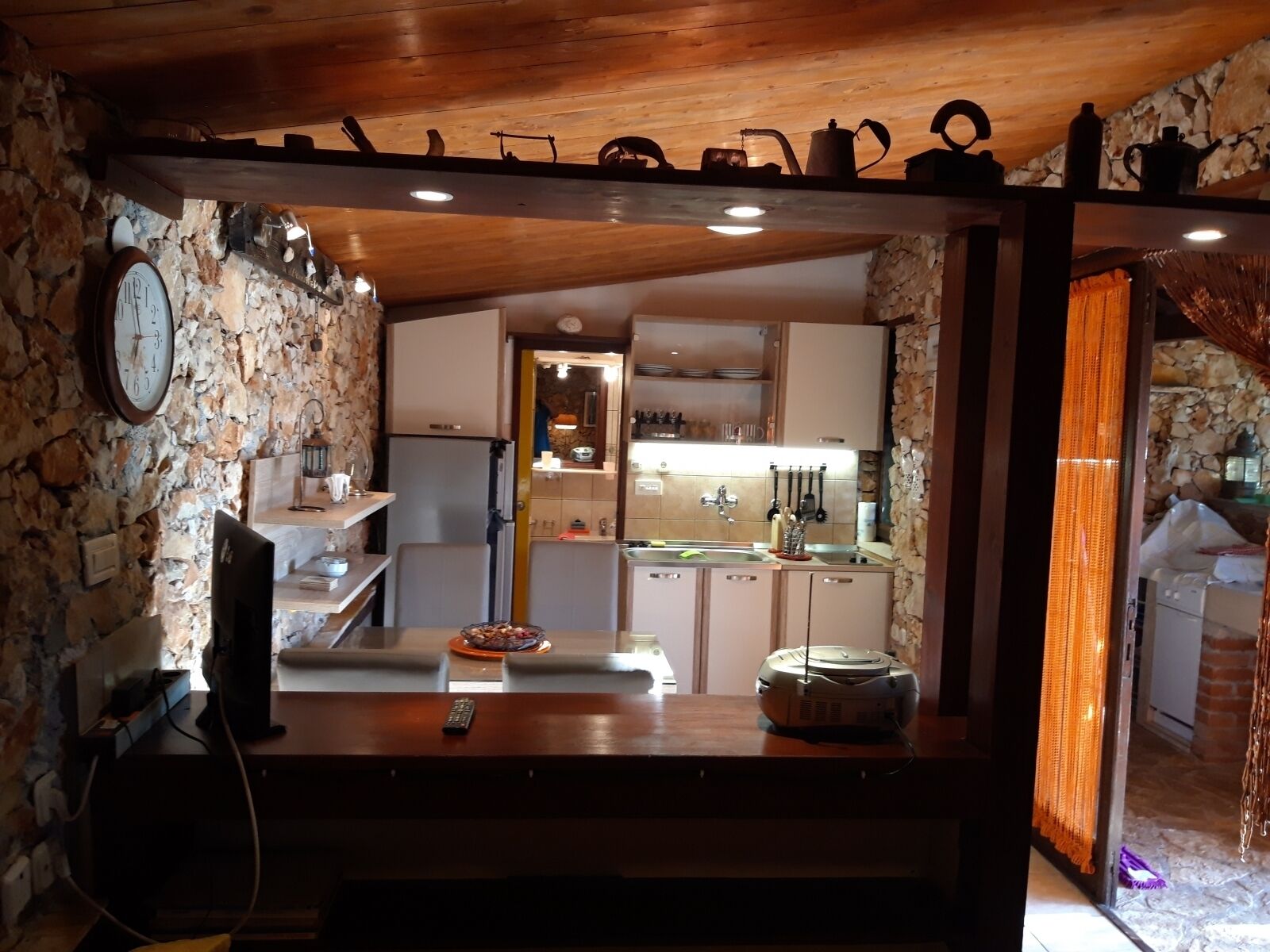 A rustic kitchen with stone walls, wooden ceiling, and a dining area with a table and chairs.