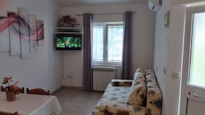 A living room with a sofa, a TV mounted on the wall, a dining table with chairs, and a window with curtains. - Apartment in Medulin with Seaview, Balcony, Air condition, WIFI (112-5) (Medulin)
