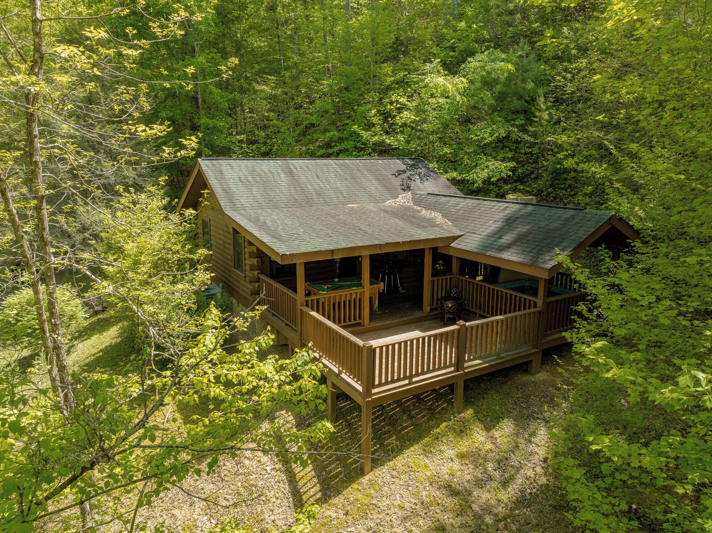 A cabin with a porch and a deck, surrounded by dense forest.