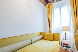 A room with a yellow sofa, a small side table with a lamp, and a window with yellow curtains.