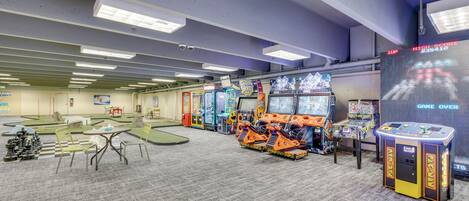 Un espace de jeux comprenant plusieurs bornes d’arcade, un jeu d’échecs et une table avec des chaises.