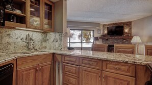 A kitchen with wooden cabinets, granite countertops, a built-in stove, and a large window offering a view of the outdoors. - Ski in/Ski Out! In Room Jacuzzi! (Breckenridge)