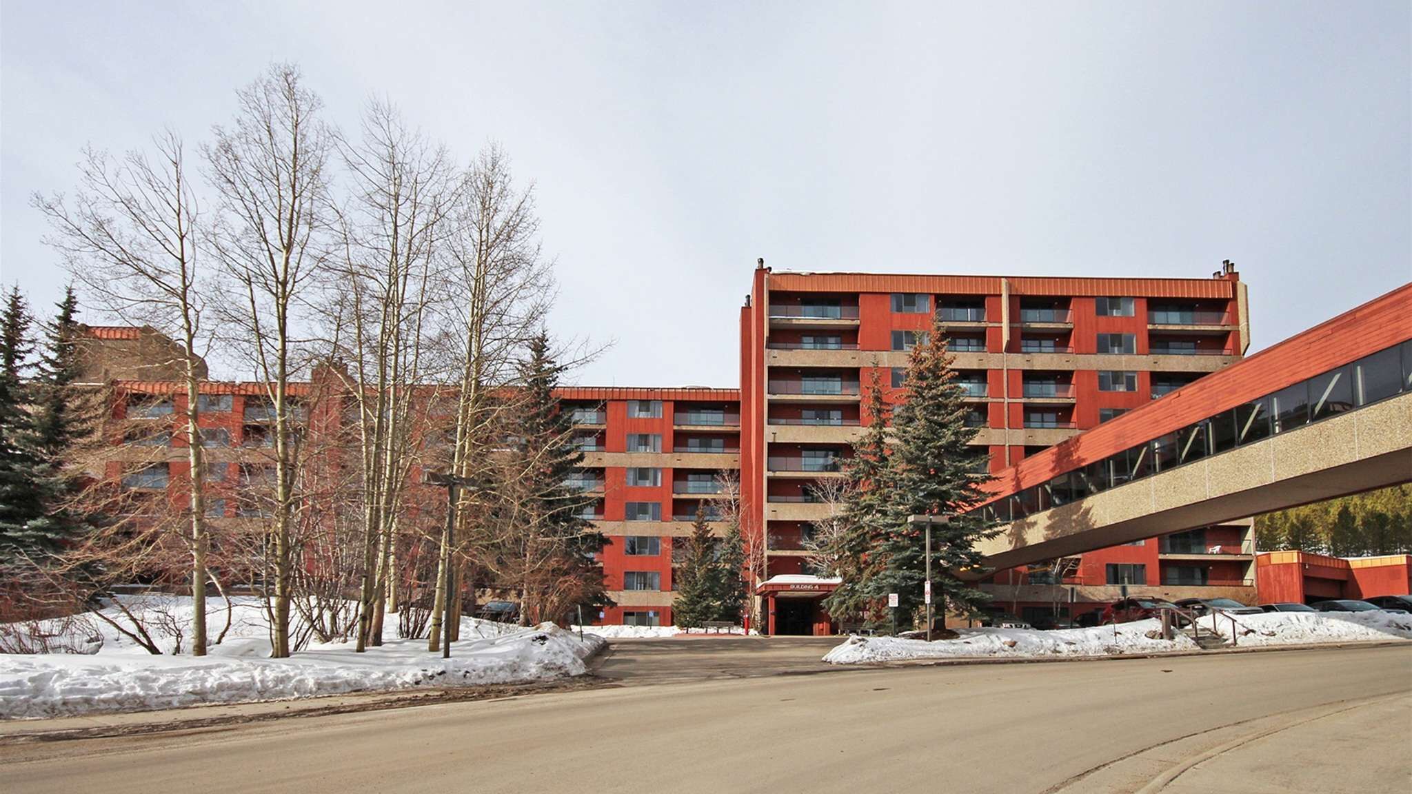 Un immeuble à plusieurs étages avec une façade rouge, une galerie couverte et de la neige au sol.