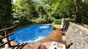 Ett trädäck med en swimmingpool, omgivet av frodig grönska och en stenmur.