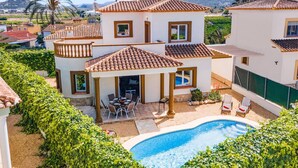 Une maison à deux étages avec une piscine, entourée de verdure et de palmiers.