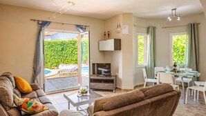 Un salon comprenant un canapé, un téléviseur et un coin repas avec une table et des chaises.