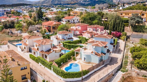 Un quartier résidentiel où les maisons se distinguent par leurs toits recouverts de tuiles rouges, une piscine et un paysage montagneux en arrière-plan.