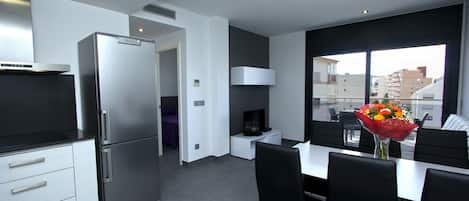 A modern kitchen with a built-in refrigerator, a dining area with a table and chairs, and a large window offering a city view.