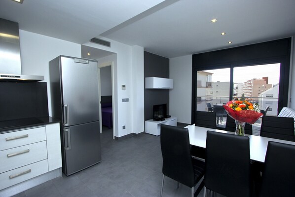 A modern kitchen with a built-in refrigerator, a dining area with a table and chairs, and a large window offering a city view.