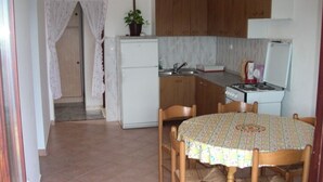 A compact kitchen with wooden cabinets, a white refrigerator, a gas stove, and a dining table with four chairs. - Apartment in Lokva Rogoznica with Seaview, Balcony, Air condition, WIFI (88-1) (Lokva Rogoznica)