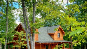 Una baita di legno con un portico e un piccolo patio, circondata da alberi.