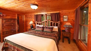 Camera da letto in una baita di legno, con un letto, una cassettiera, una lampada e una finestra.
