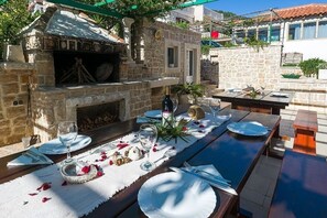 Un espace de restauration en plein air doté d’un four en pierre, avec une table dressée pour deux personnes, comprenant des assiettes, des verres et des couverts.