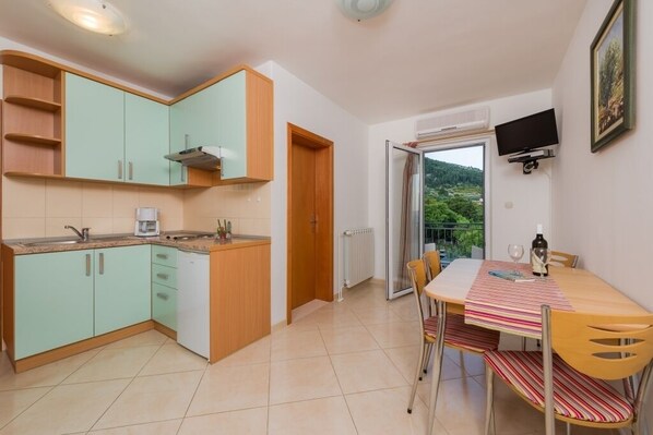 Une cuisine compacte avec des meubles de couleur turquoise, un plan de travail en bois et un coin repas comprenant une table et des chaises.