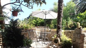 An outdoor patio area with stone walls, a table and chairs, a hanging plant, and a tire planter. - Apartment in Veli Lošinj with Terrace, Air condition, WIFI, Washing machine (63-2) (Veli Lošinj)