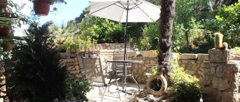 An outdoor patio area with stone walls, a table and chairs, a hanging plant, and a tire planter.