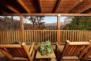 Eine Holzterrasse mit Tisch und Stühlen, einem Blumentopf und Blick auf Bäume und Berge.