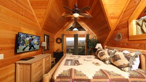 Un dormitorio acogedor con techo de madera, una cama con colcha, un televisor en la pared y vistas al exterior.