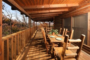 A wooden deck with tables and chairs, overlooking a forested area.