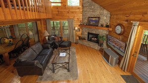 Interior acogedor de una cabaña con chimenea de piedra, mobiliario de madera y un balcón.