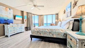 A bedroom with a large bed, a dresser, a ceiling fan, and a view of the ocean. - Tower III, 7th floor Beachfront Master (Panama City Beach)