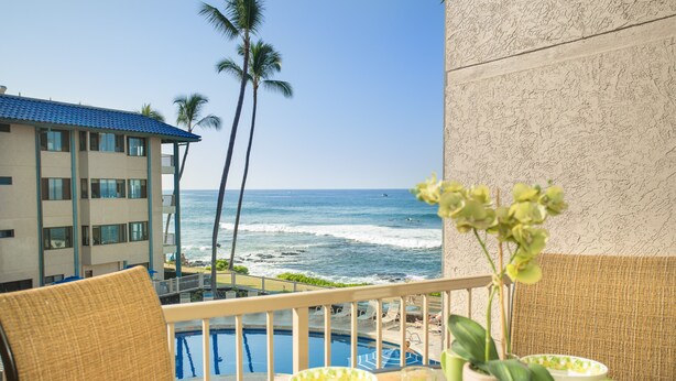 A balcony with a pool, overlooking the ocean and a hotel building. - Newly Renovated Ocean View Condo 🐳 Stunning Views From The Lanai! 🌅 Kona Reef E-22 (Kailua-Kona)