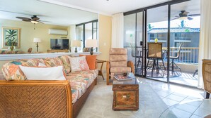 A spacious living area with a sofa, armchairs, a coffee table, and a balcony with a dining set. - Newly Renovated Ocean View Condo 🐳 Stunning Views From The Lanai! 🌅 Kona Reef E-22 (Kailua-Kona)