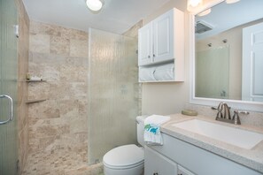 Un baño con ducha, inodoro, lavamanos y armarios.
