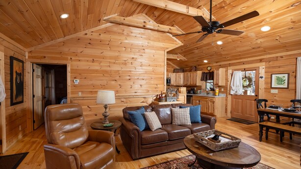 A cozy log cabin interior with a leather recliner, a brown leather sofa with blue cushions, a dining table, and a ceiling fan. - Walking Distance to Pool, Putt Putt, Fishing, Ping Pong & more! (Sevierville)