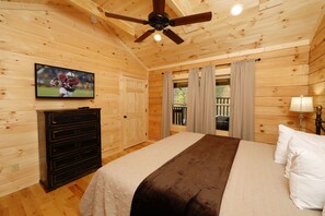 Une chambre aux murs lambrissés, comprenant un lit, une commode, un téléviseur et un ventilateur de plafond.