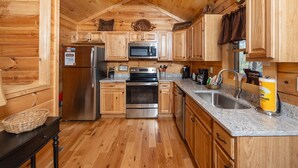 A wooden cabin-style kitchen with a refrigerator, microwave, stove, and sink. - Walking Distance to Pool, Putt Putt, Fishing, Ping Pong & more! (Sevierville)
