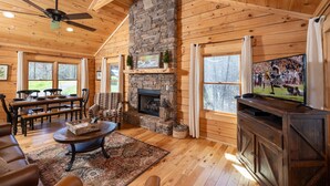A cozy log cabin interior with a stone fireplace, wooden furniture, and a television. - Walking Distance to Pool, Putt Putt, Fishing, Ping Pong & more! (Sevierville)
