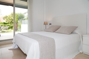 A bedroom with a large bed, a bedside table with a lamp, and a view of a patio with outdoor furniture. - Amazing round floor apartment for families - UHC SALOU VILLA 302 (Salou)