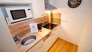 A compact kitchen with a microwave, stove, sink, and a clock on the wall. - Deluxe Studio Kaprun TOP 23 (Kaprun)
