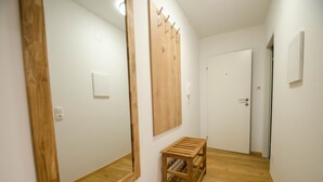 A hallway with wooden flooring, a wooden bench, a large mirror, and a door with a coat rack. - Deluxe Studio Kaprun TOP 23 (Kaprun)