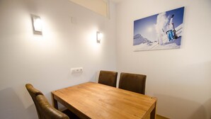 A dining area with a wooden table and four brown chairs, a wall-mounted light, and a painting of a skier. - Deluxe Studio Kaprun TOP 23 (Kaprun)