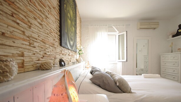 Una camera da letto con parete in mattoni, un letto con biancheria bianca, un comodino con una lampada e una finestra con tende.