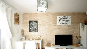 Un soggiorno moderno con parete in pietra, televisione a schermo piatto, tavolo da pranzo con sedie e oggetti decorativi.